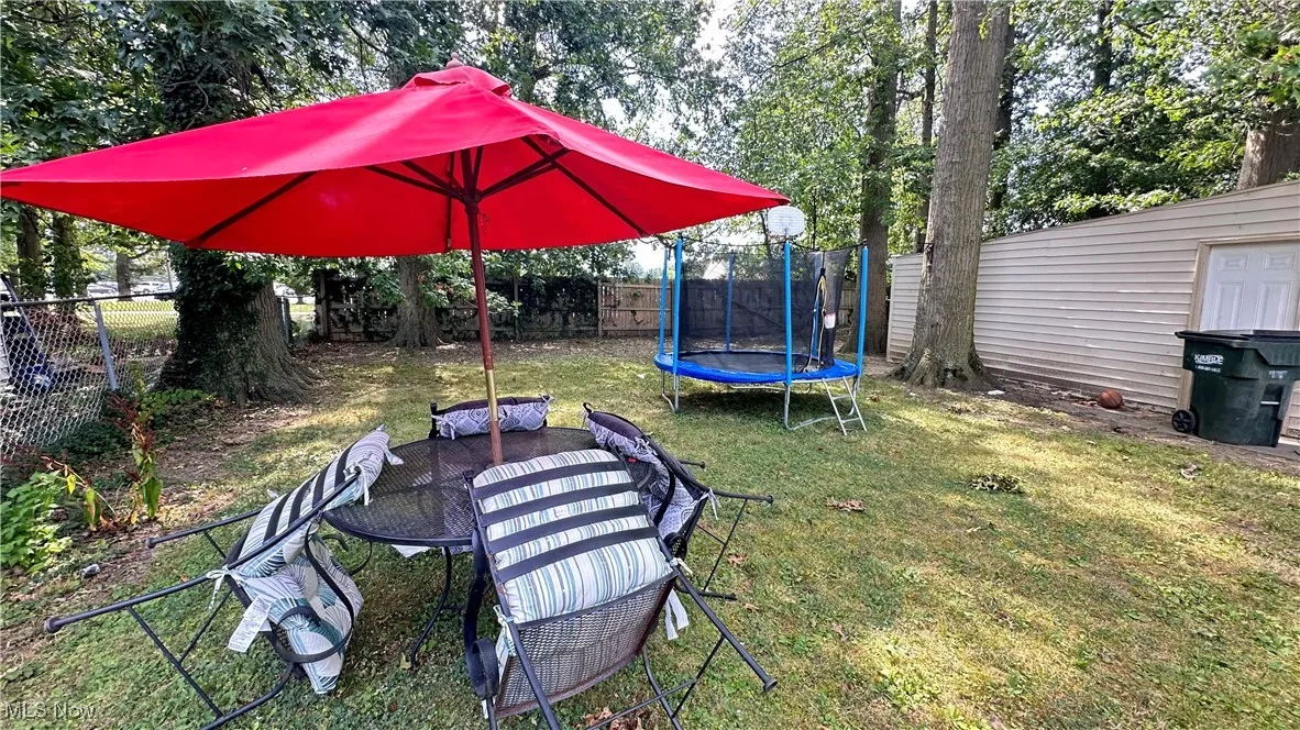 Fenced backyard featuring a trampoline and view of wooded area