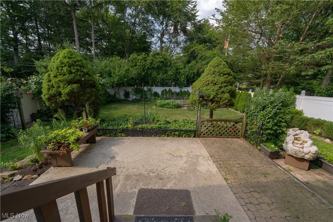 Fenced backyard with a patio area and view of scattered trees, various flowers and grape vinyard
