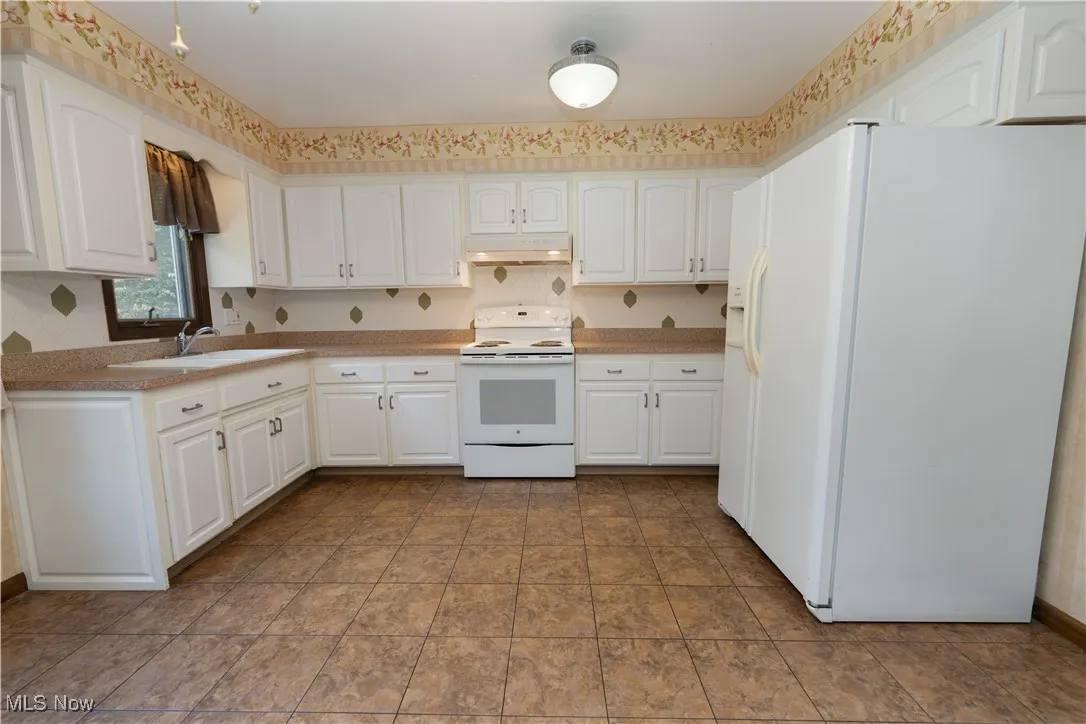Kitchen featuring white appliances, under cabinet range hood, white cabinetry, and decorative backsplash