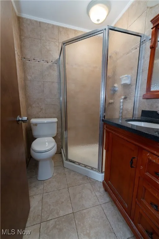 Master Bathroom featuring shower stall, vanity with granite countertop, tile walls, tile patterned floors, and ornamental molding