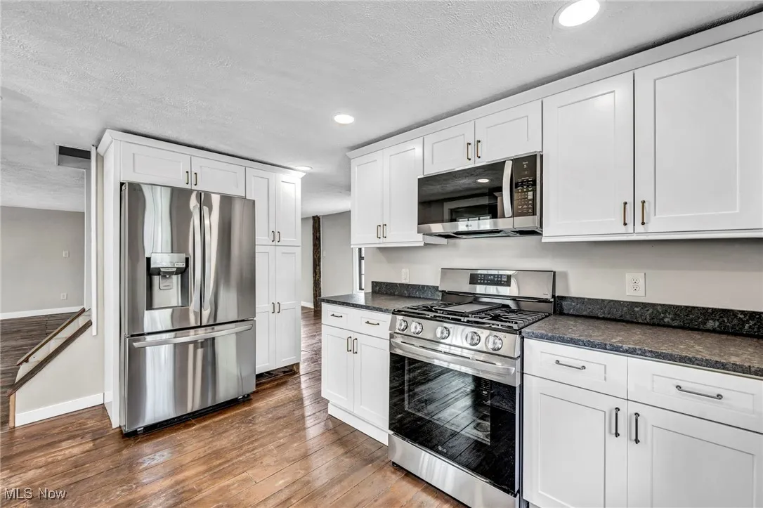 Kitchen featuring stainless steel appliances, dark countertops, dark wood-style floors, a textured ceiling, and white cabinets