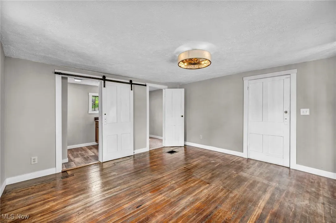 Unfurnished bedroom with a barn door, a textured ceiling, and wood finished floors