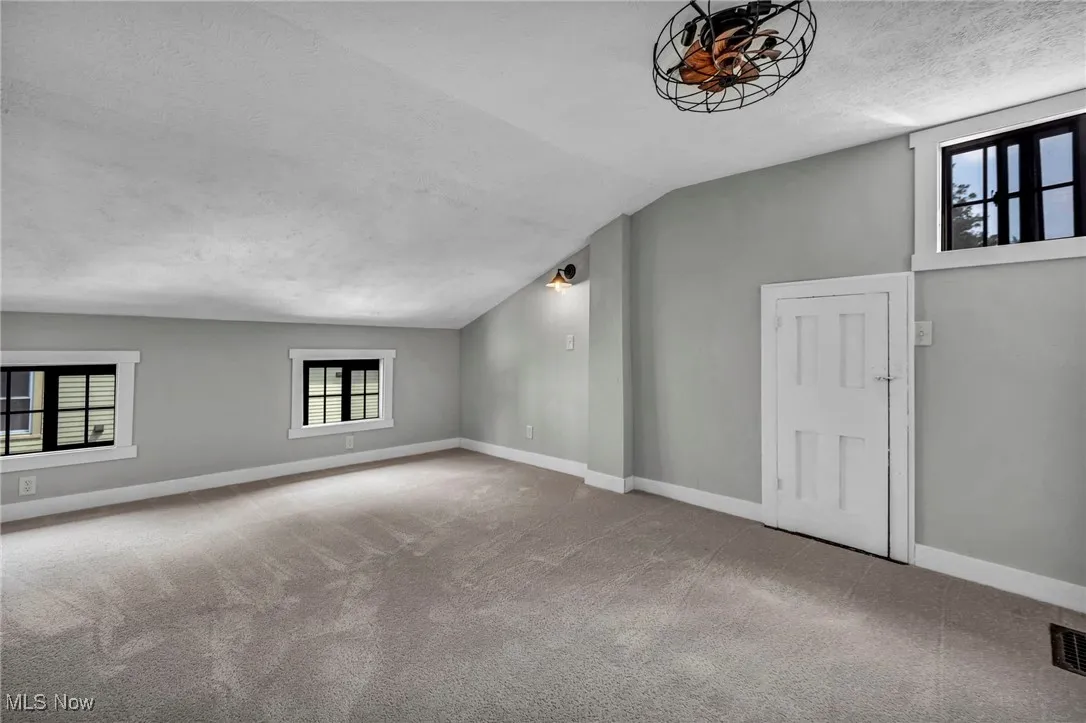 Carpeted spare room with healthy amount of natural light, a textured ceiling, and vaulted ceiling