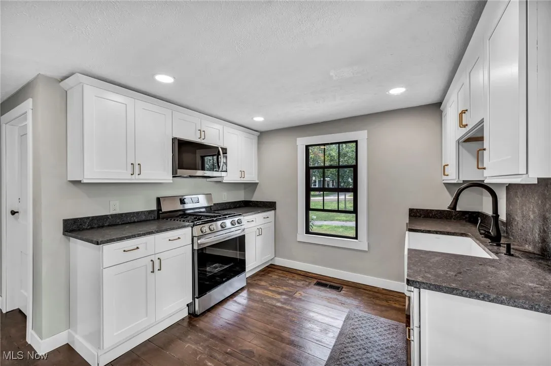 Kitchen with stainless steel appliances, dark countertops, dark wood-style floors, white cabinetry, and recessed lighting