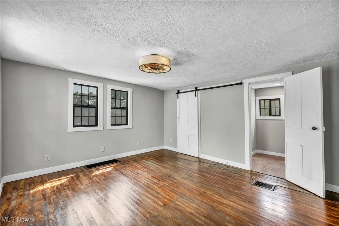 Unfurnished bedroom featuring a barn door, multiple windows, a textured ceiling, and wood-type flooring