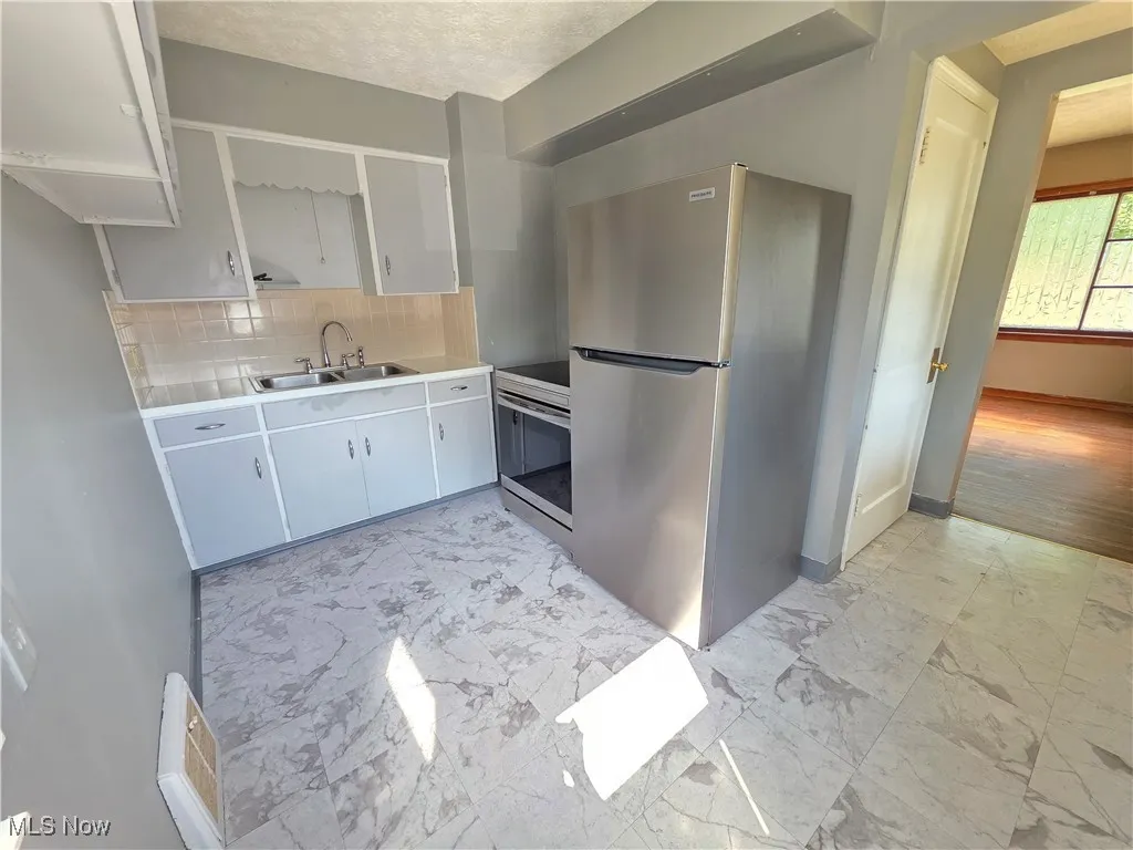 Kitchen featuring appliances with stainless steel finishes, light marble finish floors, decorative backsplash, and light countertops