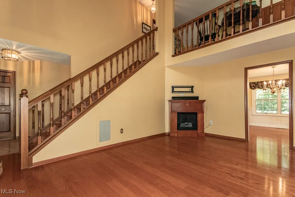 Unfurnished living room with a chandelier, a fireplace, wood finished floors, stairway, and a high ceiling