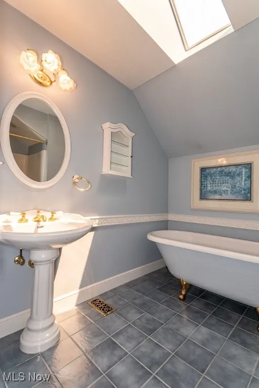 Full bathroom with lofted ceiling, a freestanding bath, a skylight, and tile patterned floors