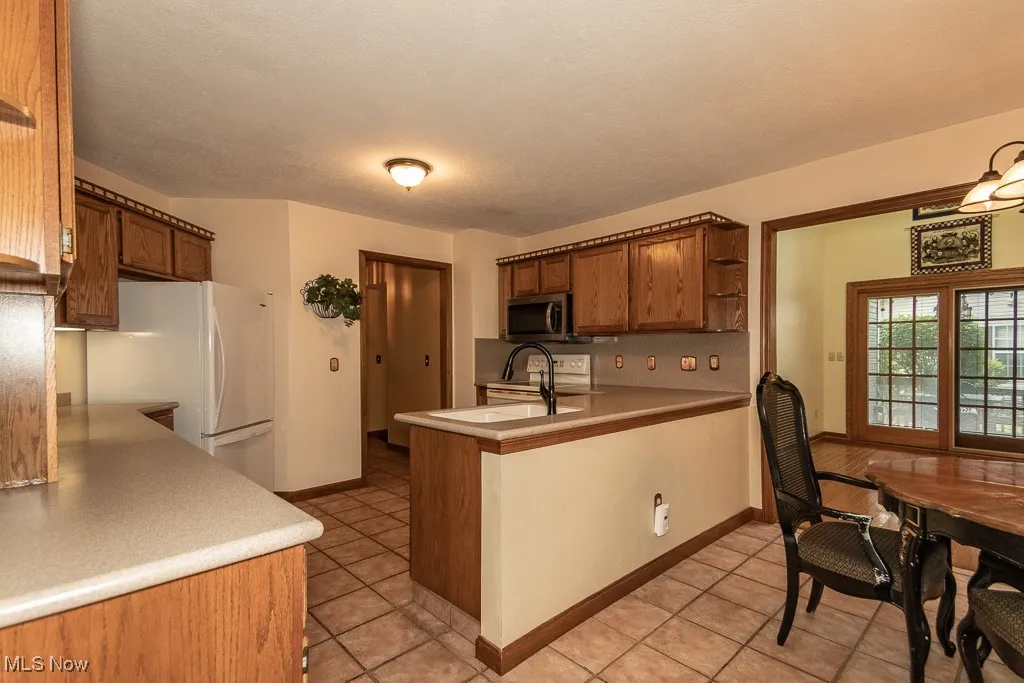 Kitchen featuring a peninsula, white appliances, light tile patterned flooring, open shelves, and a textured ceiling