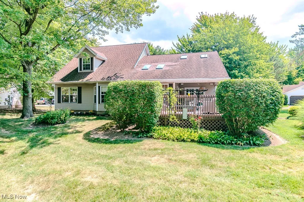 View of front of home featuring a shingled roof, a front yard, and a deck