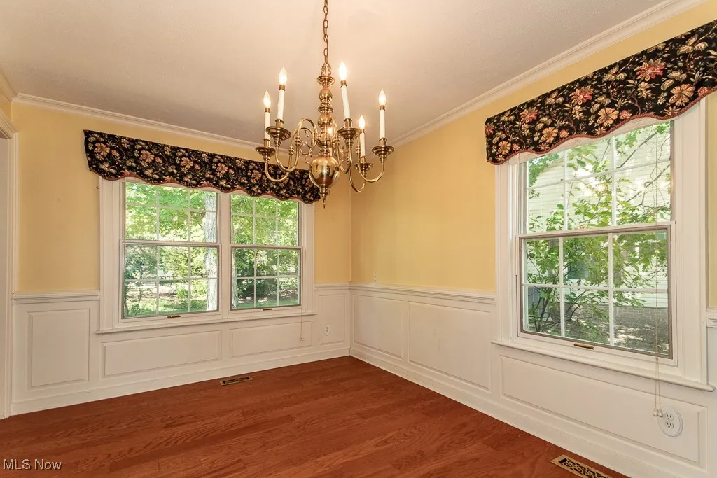 Spare room featuring a chandelier, ornamental molding, healthy amount of natural light, dark wood-style flooring, and a decorative wall