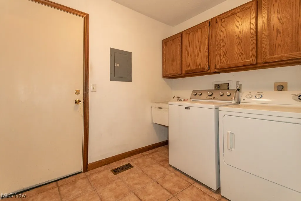 Washroom featuring cabinet space, washer and clothes dryer, electric panel, and light tile patterned floors