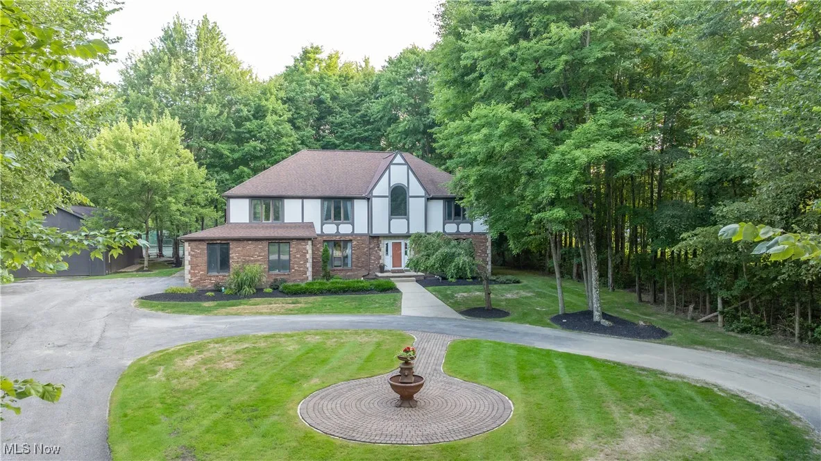Tudor home featuring brick siding, curved driveway, a front lawn, and a shingled roof