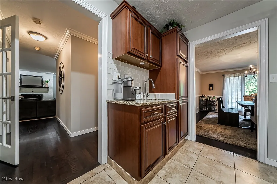 Kitchen with coffee bar/prep sink has ornamental molding, light tile patterned floors, light stone counters, and decorative backsplash