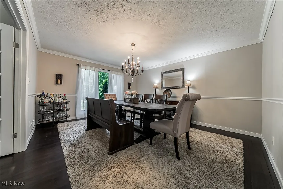 Dining area with a textured ceiling, crown molding, dark wood-style floors, and a chandelier