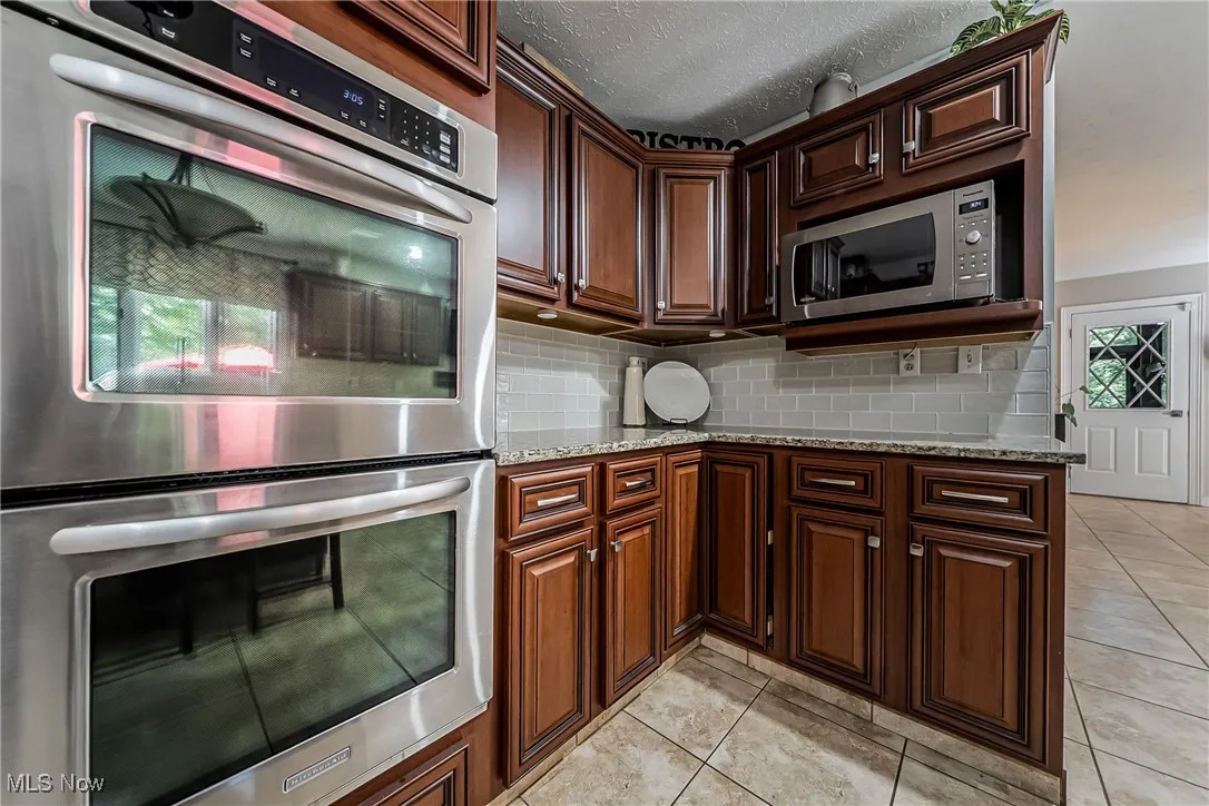 Kitchen with stainless steel appliances, tasteful backsplash, light tile flooring.