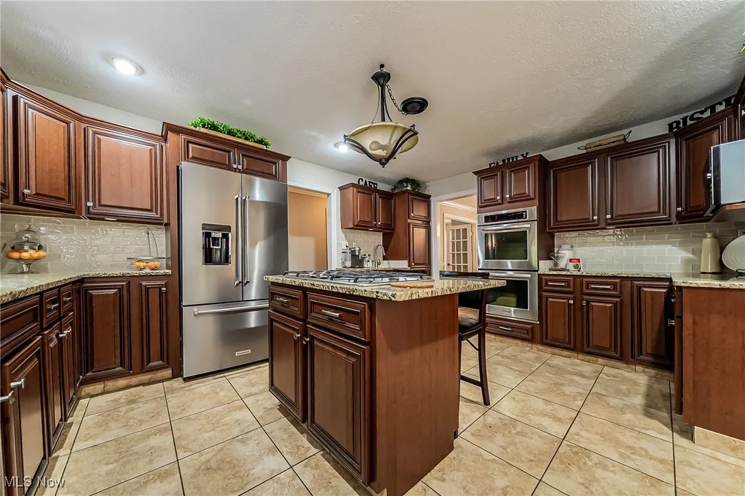 Kitchen with decorative backsplash, stainless steel appliances, 5-burner gas cooktop, light tile patterned floors, a kitchen coffee or prep bar.