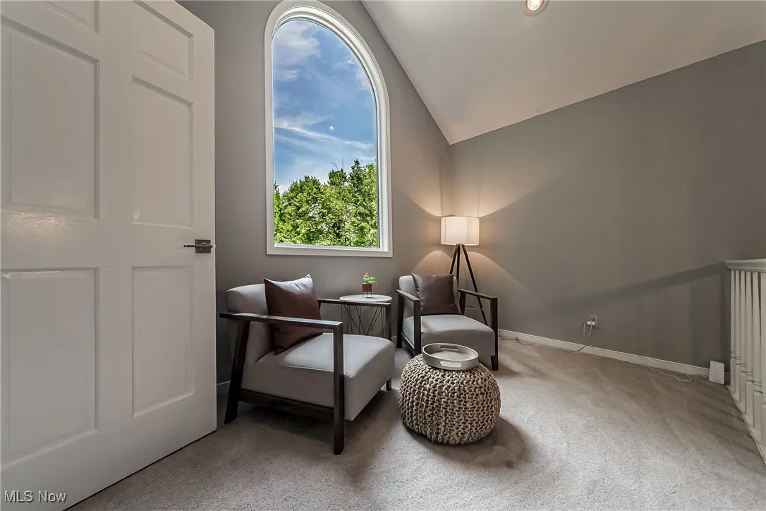 Sitting room featuring lofted ceiling and carpet flooring and large window to allow natural light inside.