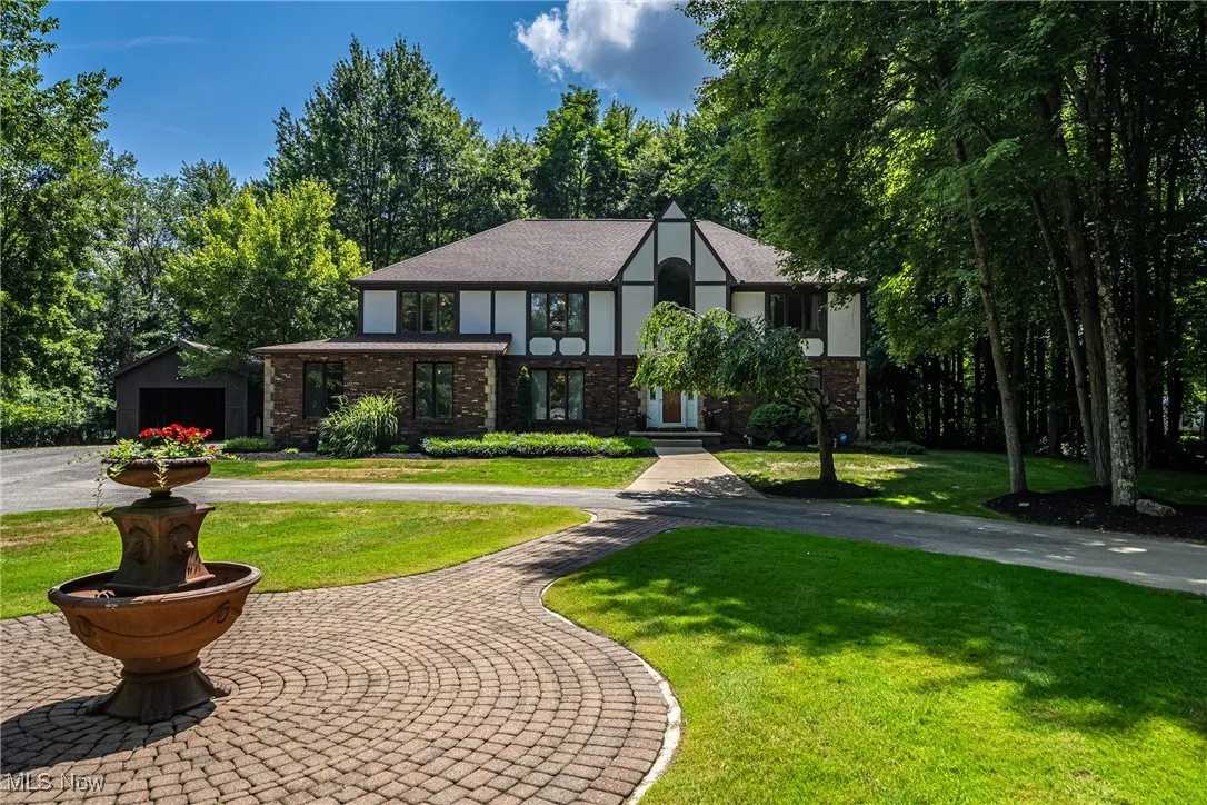 Tudor home featuring brick siding, a front yard, curved driveway, roof with shingles, and stucco siding