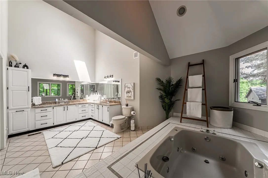 Primary bath featuring high vaulted ceiling, double vanity, a whirlpool tub, tile patterned floors, and a skylight
