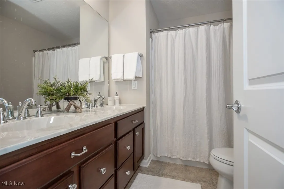 Full bathroom with double vanity, light tile patterned floors, and curtained shower