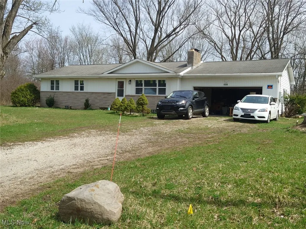 View of side of home with dirt driveway, a lawn, a chimney, and brick siding
