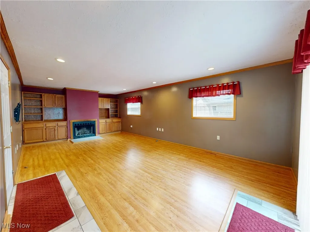 Living room featuring ornamental molding, a fireplace, recessed lighting, light wood-type flooring, and built in shelves