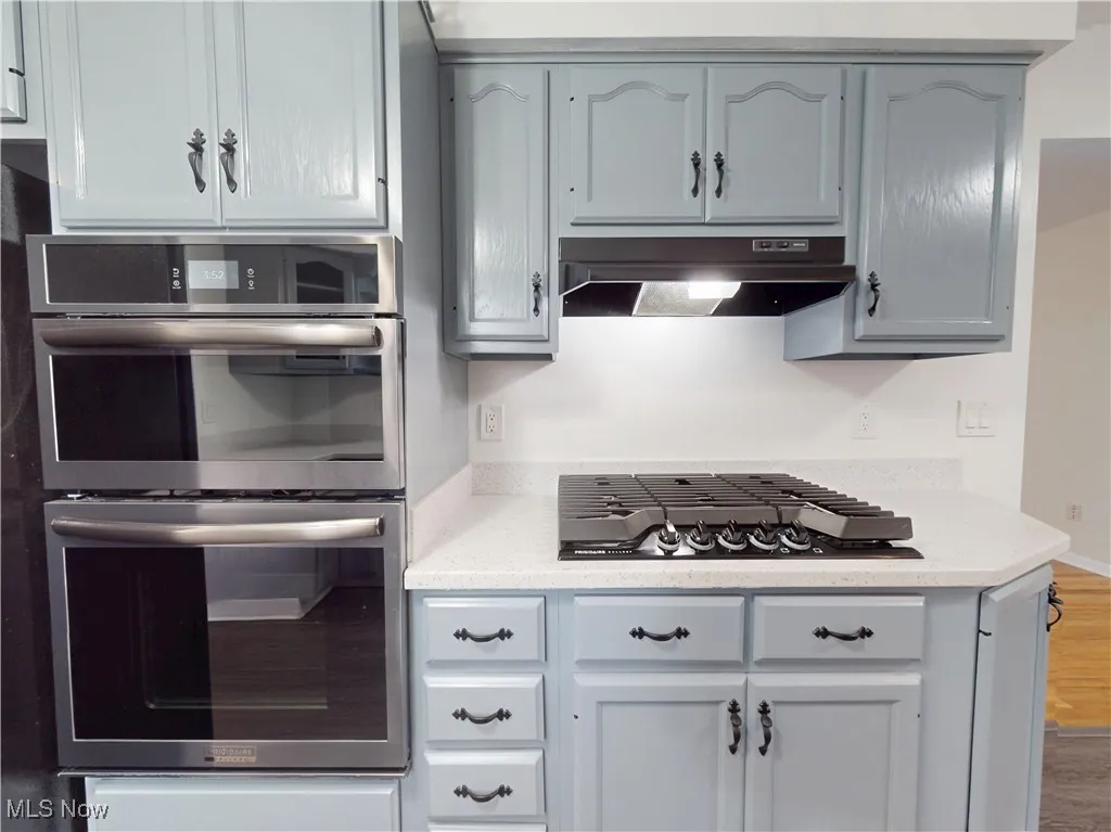Kitchen featuring stainless steel appliances, light countertops, wood finished floors, and under cabinet range hood