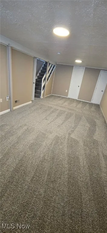 Finished below grade area with carpet floors, a textured ceiling, and stairs