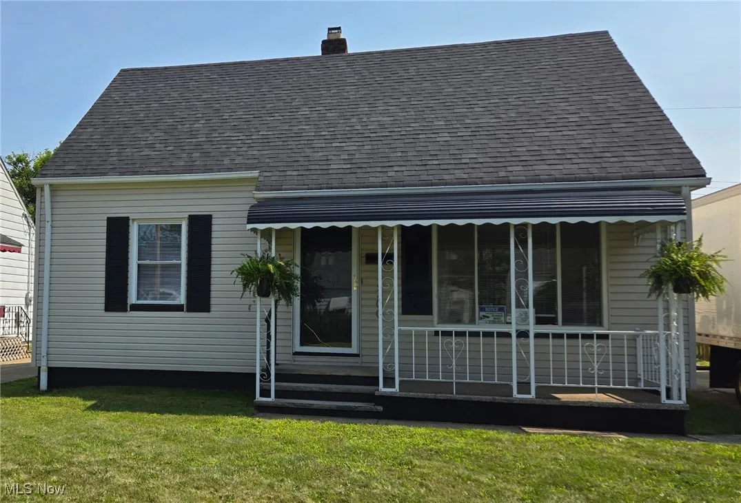 View of front of home with a chimney, roof with shingles, a front lawn, and covered porch