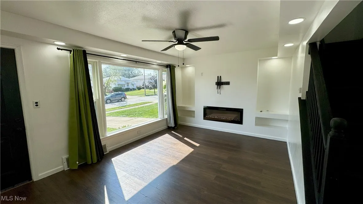 Unfurnished living room with recessed lighting, dark wood-style floors, a glass covered fireplace, stairway, and ceiling fan