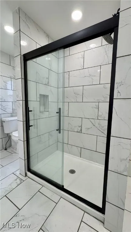 Bathroom with marble finish floors, tile walls, and a shower stall
