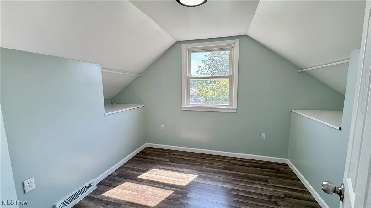 Additional living space with dark wood-type flooring and vaulted ceiling