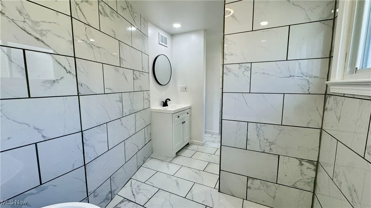 Full bathroom with vanity, tile walls, and light marble finish floors