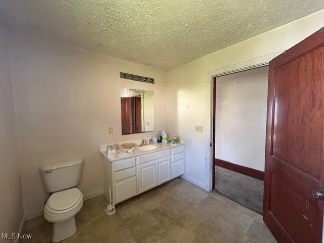 Half bath featuring a textured ceiling, vanity, and light tile patterned flooring