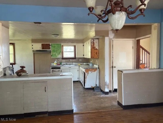 Kitchen with a peninsula, tile countertops, dark wood-style floors, white cabinetry, and extractor fan