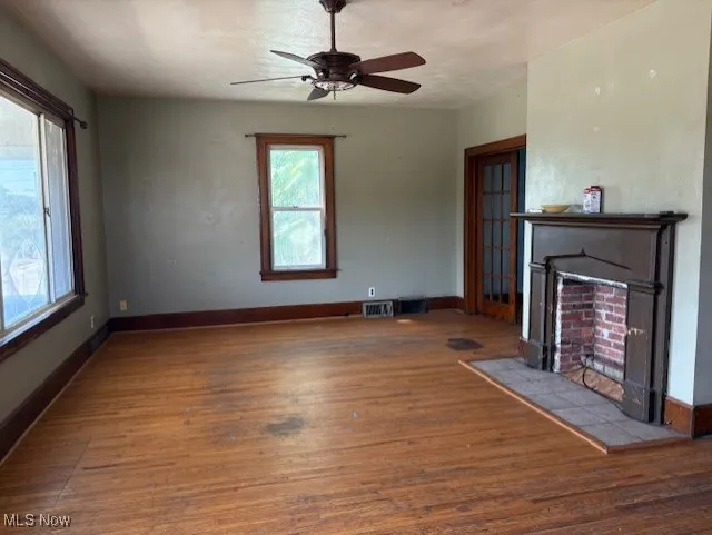 Unfurnished living room with dark wood-type flooring, a fireplace with flush hearth, and a ceiling fan