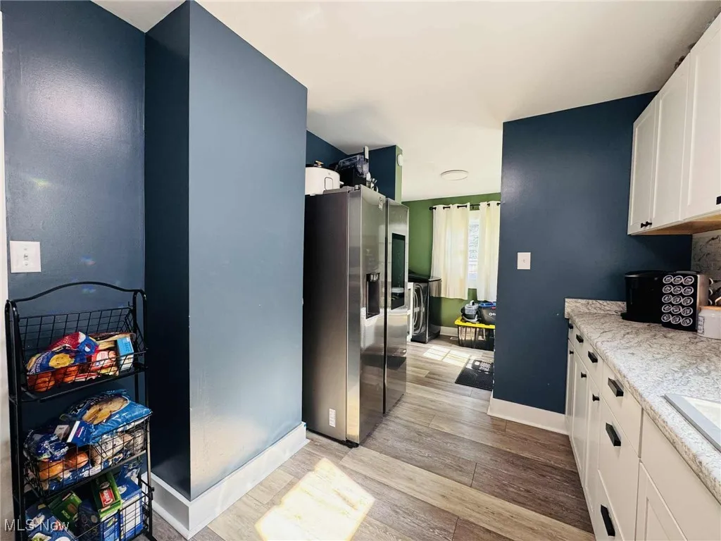 Kitchen with white cabinets, light wood-style flooring, and stainless steel refrigerator with ice dispenser