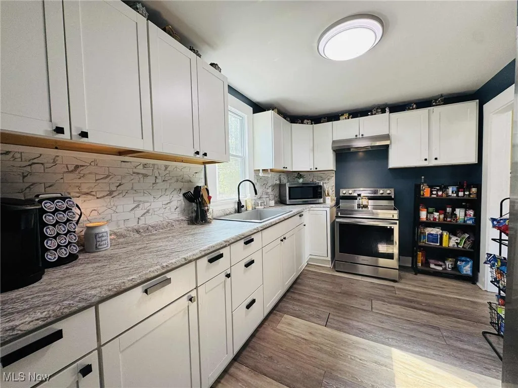 Kitchen with appliances with stainless steel finishes, white cabinets, tasteful backsplash, dark wood-style flooring, and under cabinet range hood