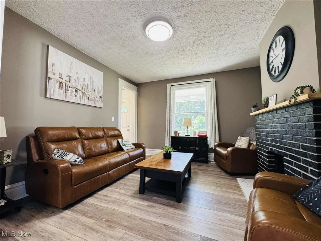 Living area with light wood-type flooring, a textured ceiling, and a brick fireplace