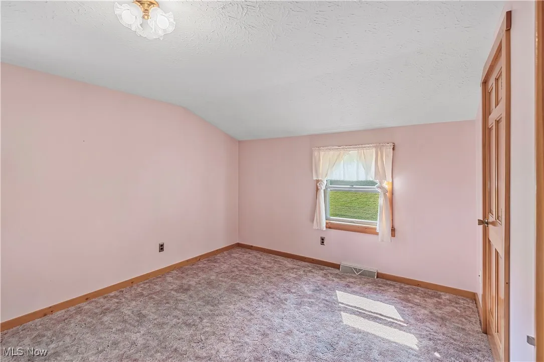 Unfurnished bedroom with lofted ceiling, carpet, and a textured ceiling