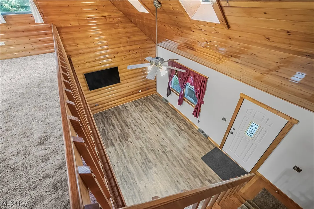 Living area with a skylight, stairway, wood finished floors, high vaulted ceiling, and ceiling fan