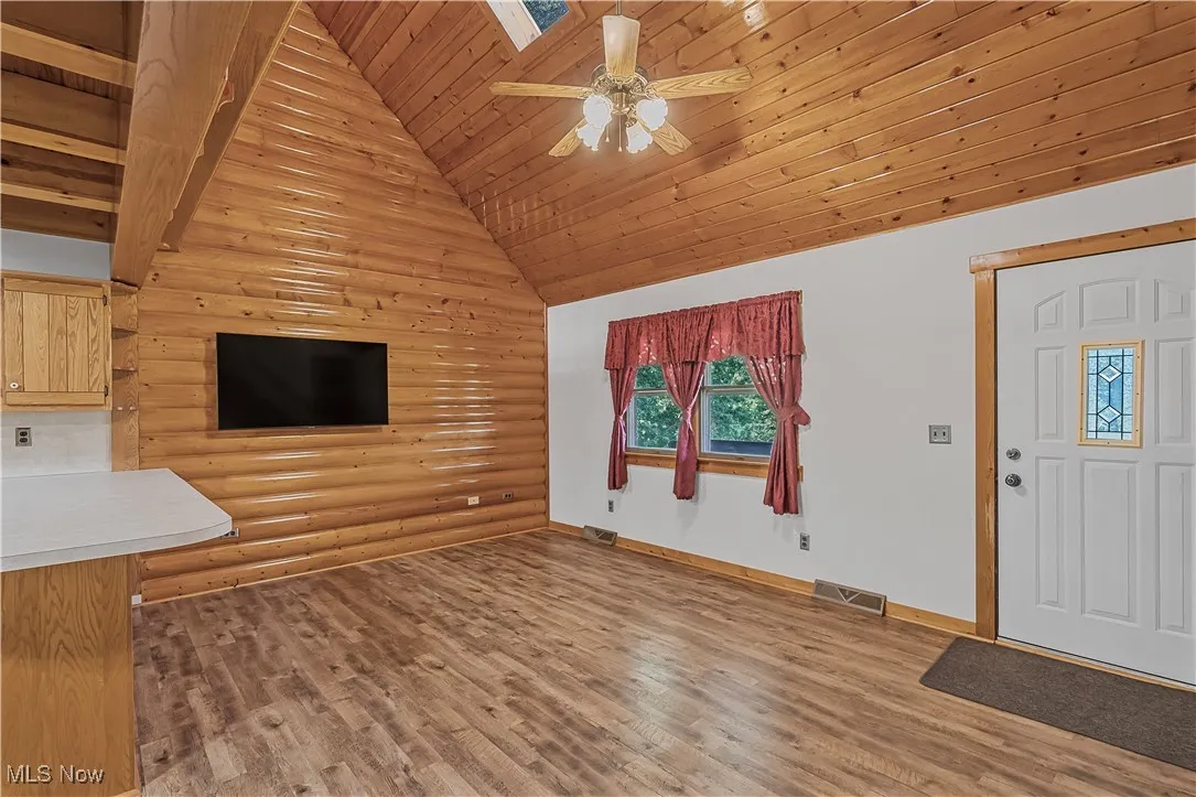 Unfurnished living room with wood ceiling, light wood finished floors, a skylight, a ceiling fan, and log walls