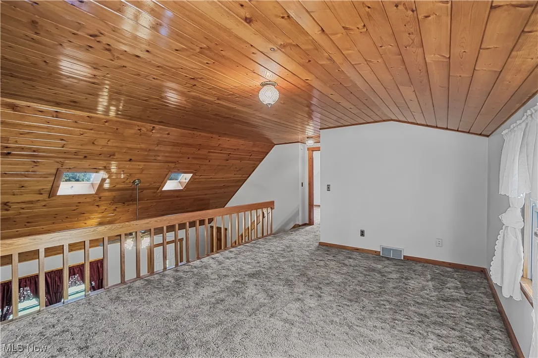 Additional living space with vaulted ceiling, carpet floors, a skylight, wooden ceiling, and plenty of natural light