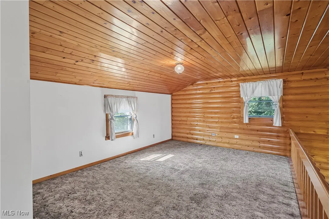 Spare room featuring vaulted ceiling, log walls, and carpet flooring