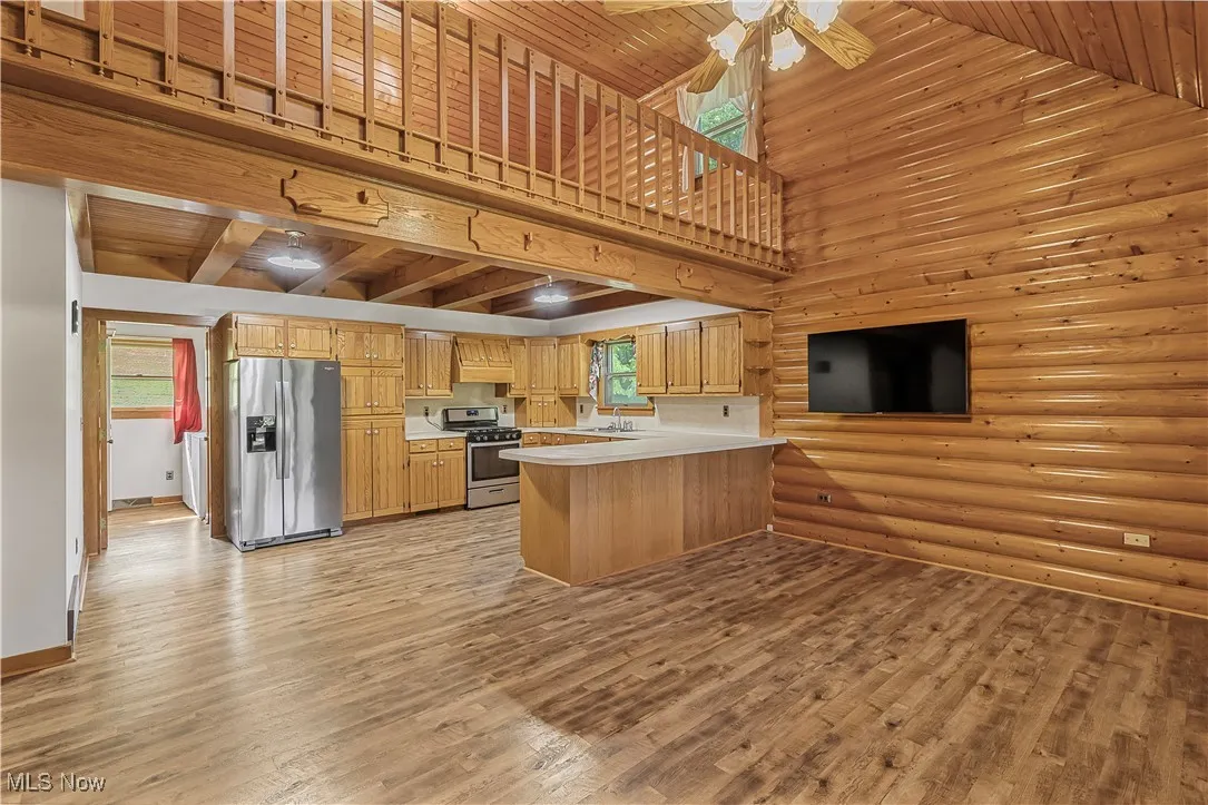 Kitchen with light countertops, appliances with stainless steel finishes, wood ceiling, log walls, and a peninsula