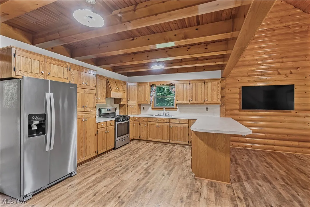 Kitchen with a peninsula, stainless steel appliances, light countertops, light wood-type flooring, and custom range hood