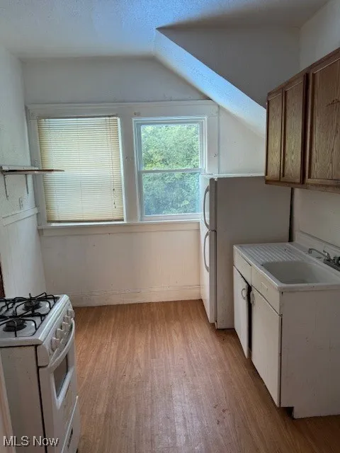 Kitchen with stove, light wood-style floors, light countertops, refrigerator, and vaulted ceiling