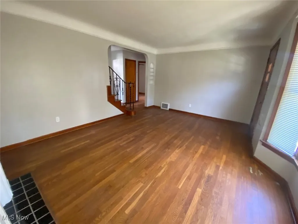 Unfurnished living room with arched walkways, stairway, and wood finished floors