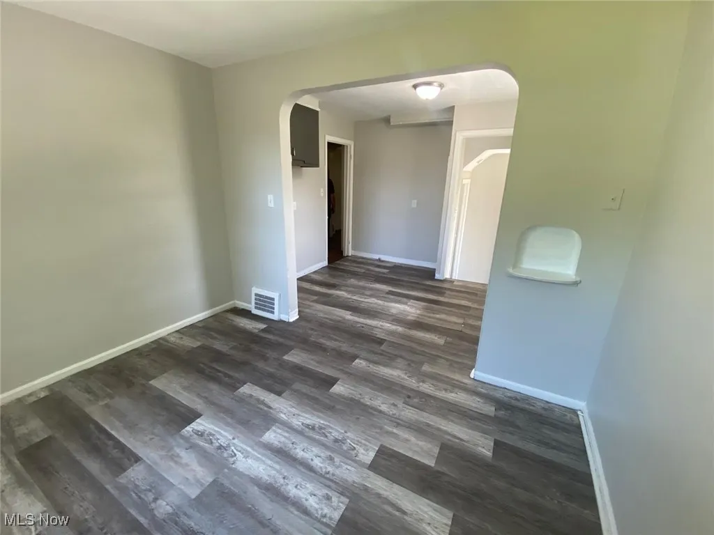 Empty room with dark wood-style flooring and arched walkways